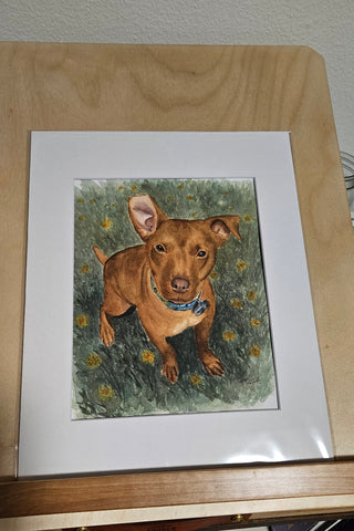 Framed artwork of a dog sitting in the grass with a collar, surrounded by flowers.